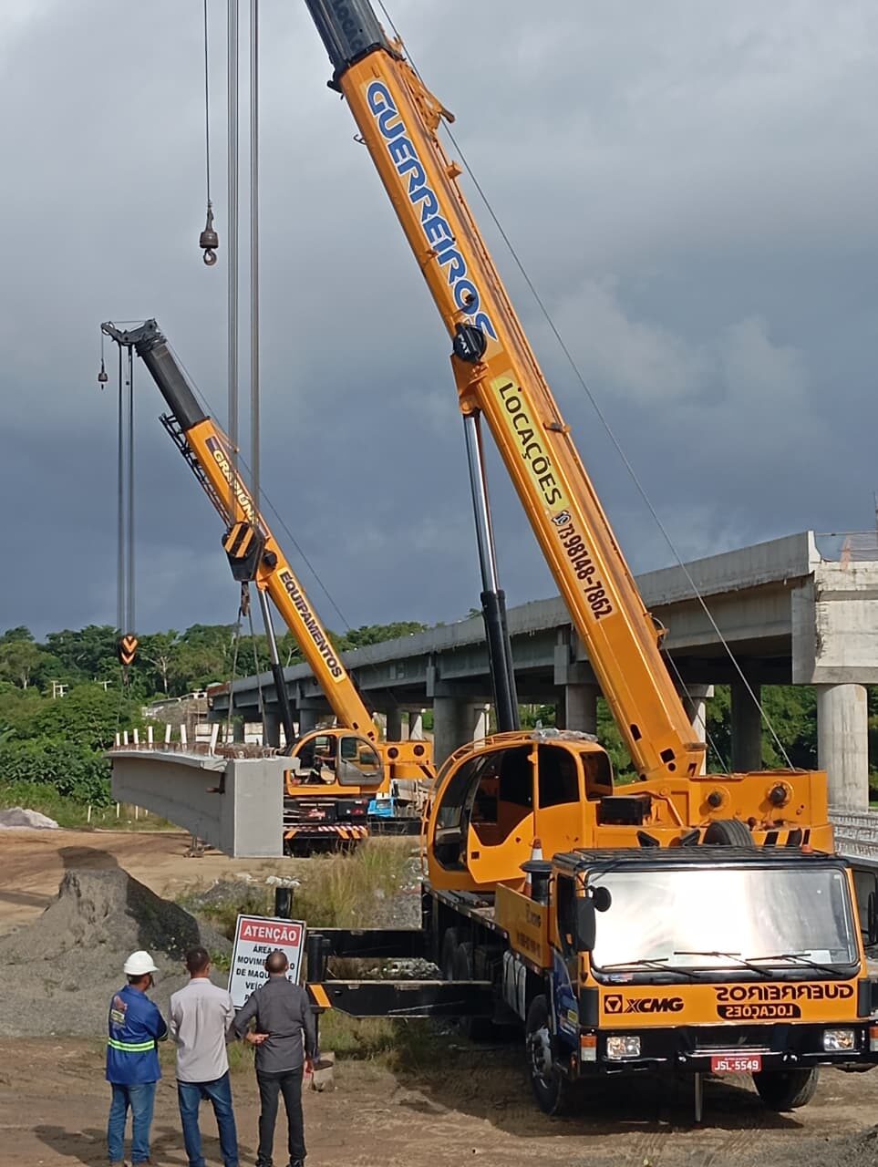 Dois guindastes içando viga de concreto em obra de ponte